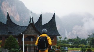 A hiker stands in front of an old asian building. Misty mountains in the background.